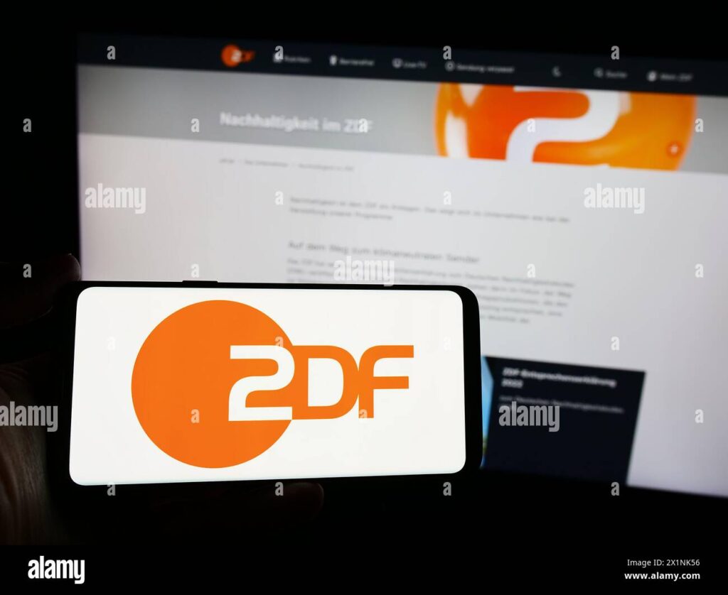 Main tenant un smartphone affichant le logo de ZDF en gros plan, symbole de la publicité télévisée